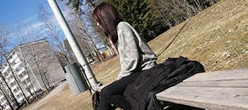 Pitkähiuksinen nainen istuu puiston penkillä.