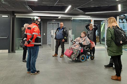 Kokemustoimijat kuuntelevat oranssitakkista ja kypärällä varustautunutta Jani Heleniusta areenalal.