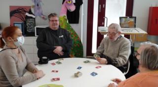 Marko pöydän ääressä pelaamassa kolmen muun ihmisen kanssa korttipeliä.