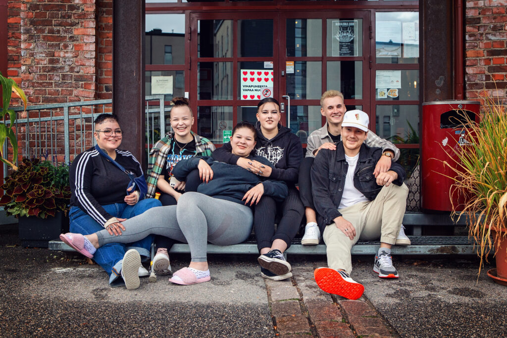 Kuusi nuorta istuu rakennuksen edessä.
