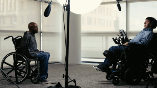 Kaksi pyörätuolissa istuvaa miestä äänistudiossa.
