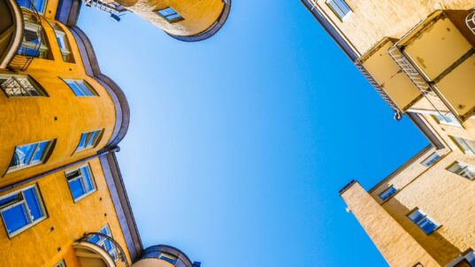 Keltaisten kerrostalojen ympäröimä sisäpiha ja sininen taivas.