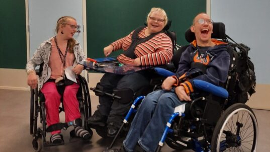 Kolme pyörätuolia käyttävää ihmistä.
