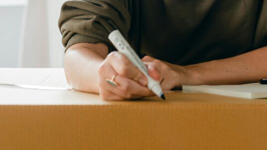 Ihminen kirjoittaa tussilla muuttolaatikkoon.