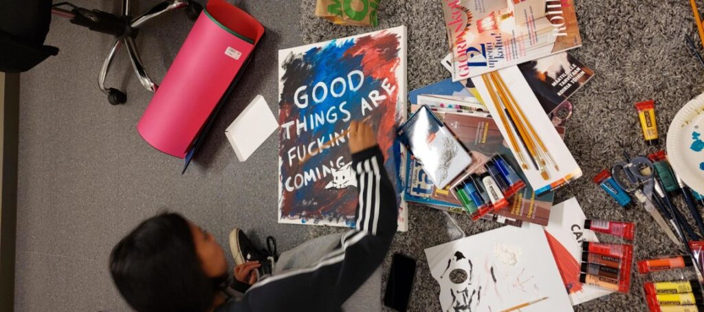 Nuori maalaa kuvaa, jossa lukee goog things are fucking coming.