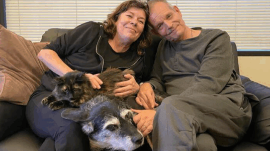 Nainen ja mies istuu sohvalla kissa ja koira sylissään.