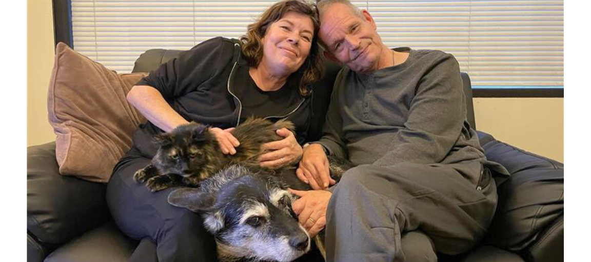 Nainen ja mies istuu sohvalla kissa ja koira sylissään.