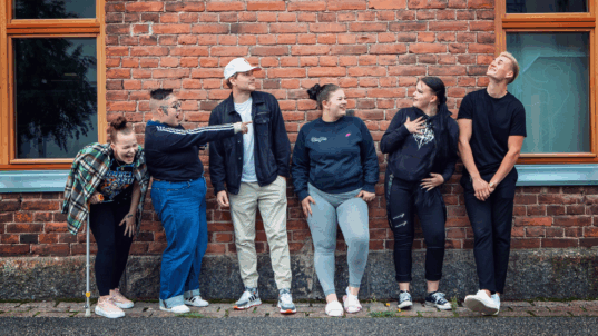 Kuusi nuorta tiiliseinän edessä.