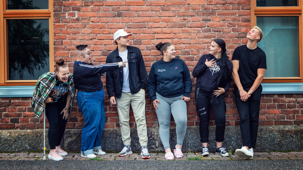 Kuusi nuorta tiiliseinän edessä.