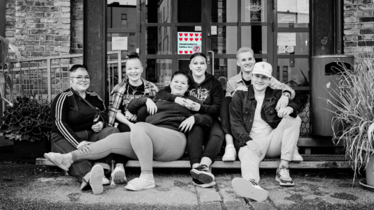 Kuusi hymyilevää nuorta istumassa portailla.