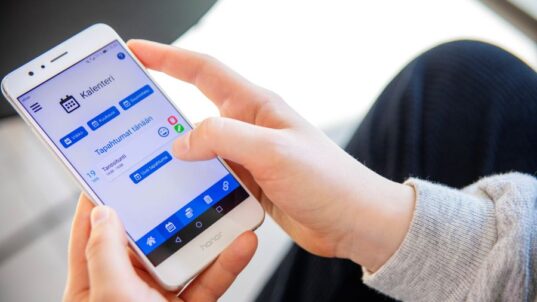 Kädet pitelevät kännykkää, joissa on auki Digihelppari-sovelluksen kalenterinäkymä.