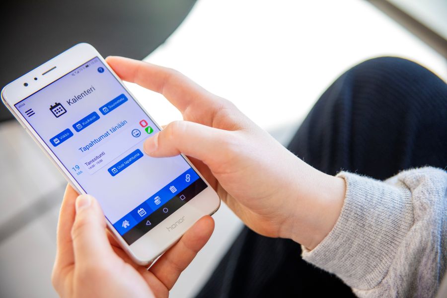 Kädet pitelevät kännykkää, joissa on auki Digihelppari-sovelluksen kalenterinäkymä.