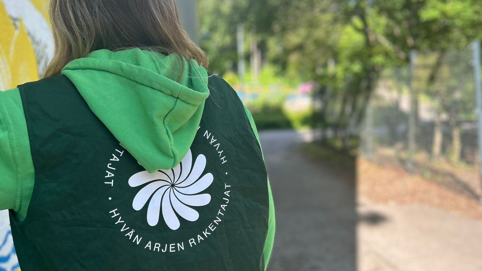 Pitkähiuksinen hainen selkä päin kameraa, hupparin selässä lukee Hyvän arjen rakentajat