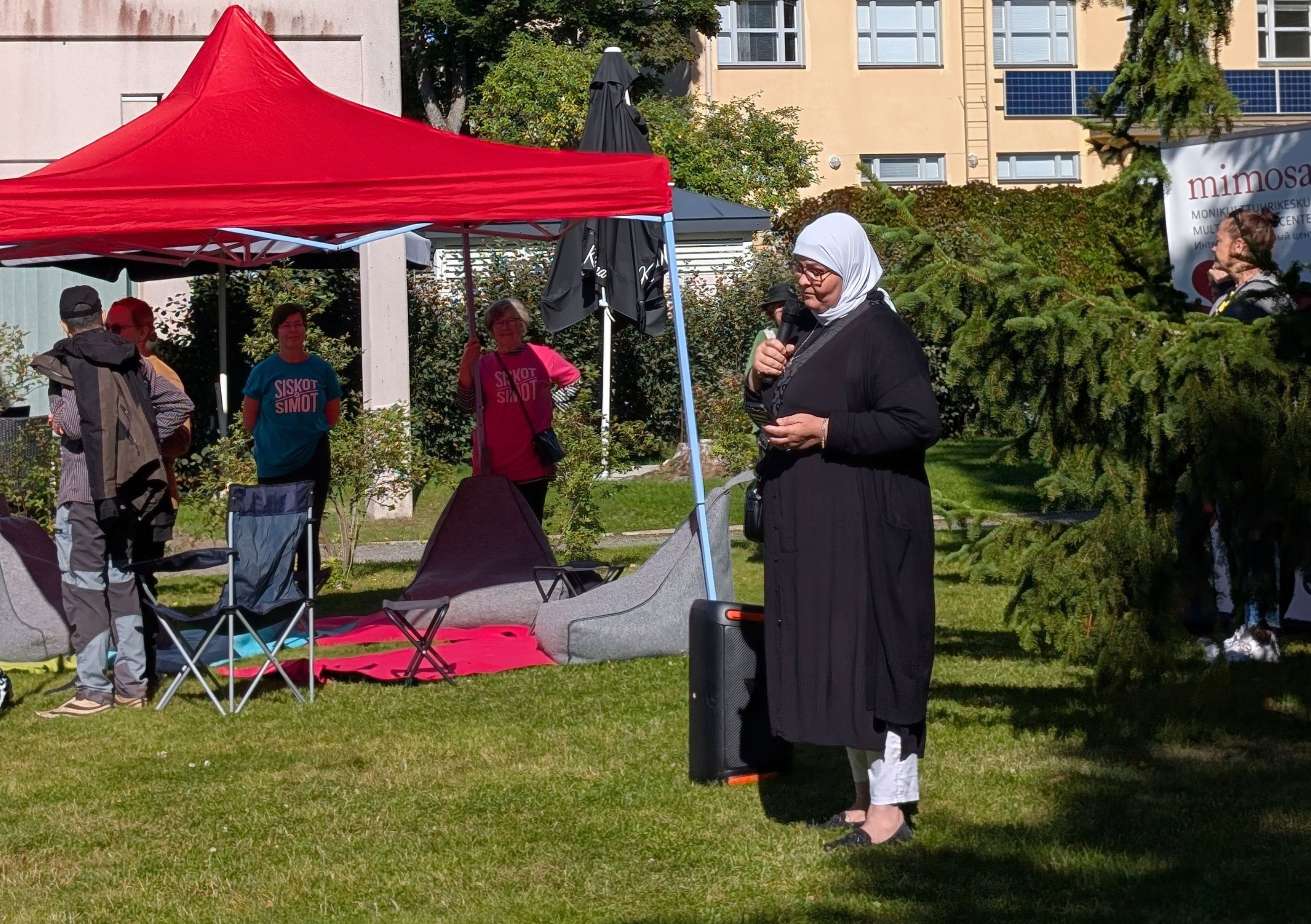 Evelina Lafghani pitää puhetta, vieressä katos, jonka alla katsojia.